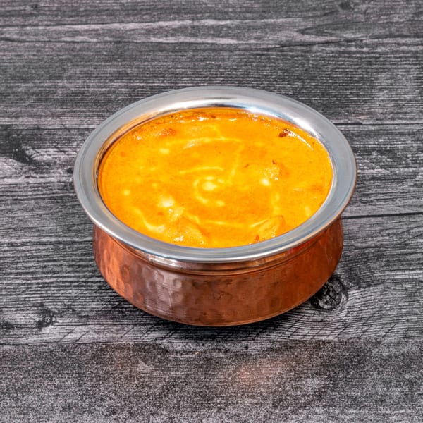 Masala Indian Cuisine's creamy orange curry in a copper and silver bowl on a dark wooden surface.