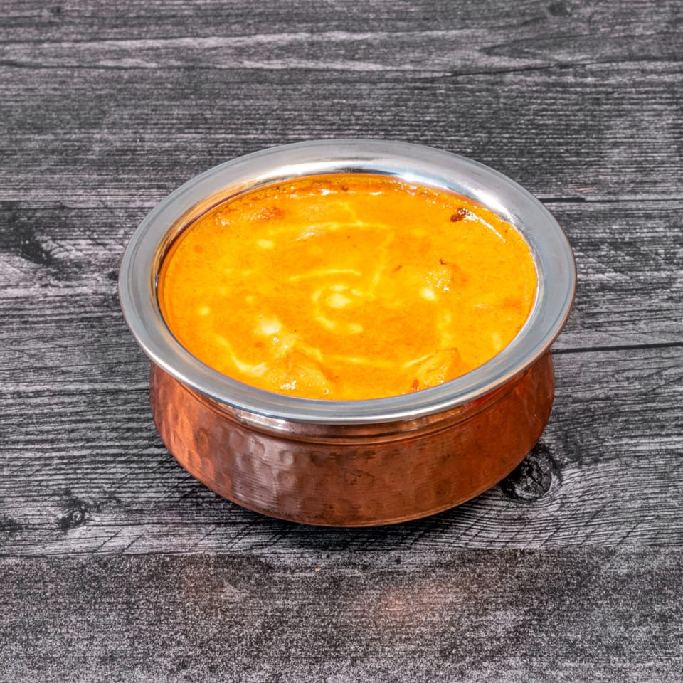 Masala Indian Cuisine's creamy orange curry in a copper and silver bowl on a dark wooden surface.