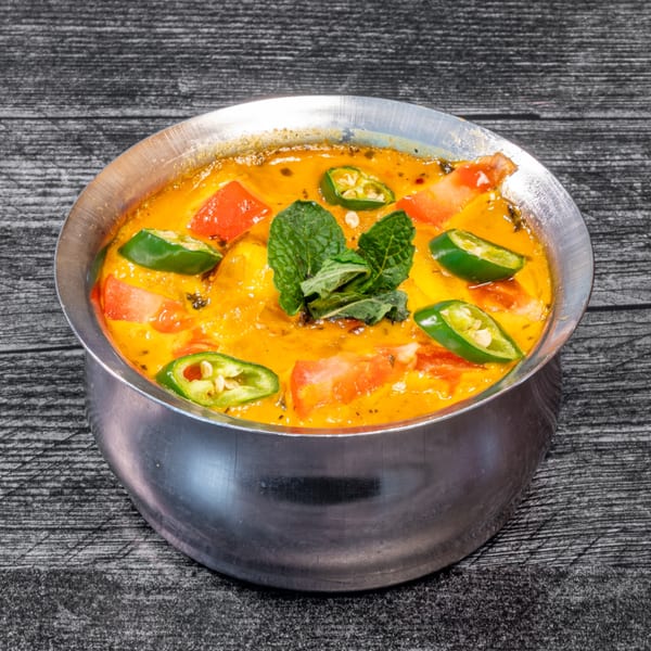 Masala Indian Cuisine's creamy yellow curry with red tomatoes, green chilies, and mint in a metal bowl.