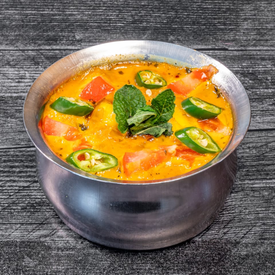 Masala Indian Cuisine's creamy yellow curry with red tomatoes, green chilies, and mint in a metal bowl.