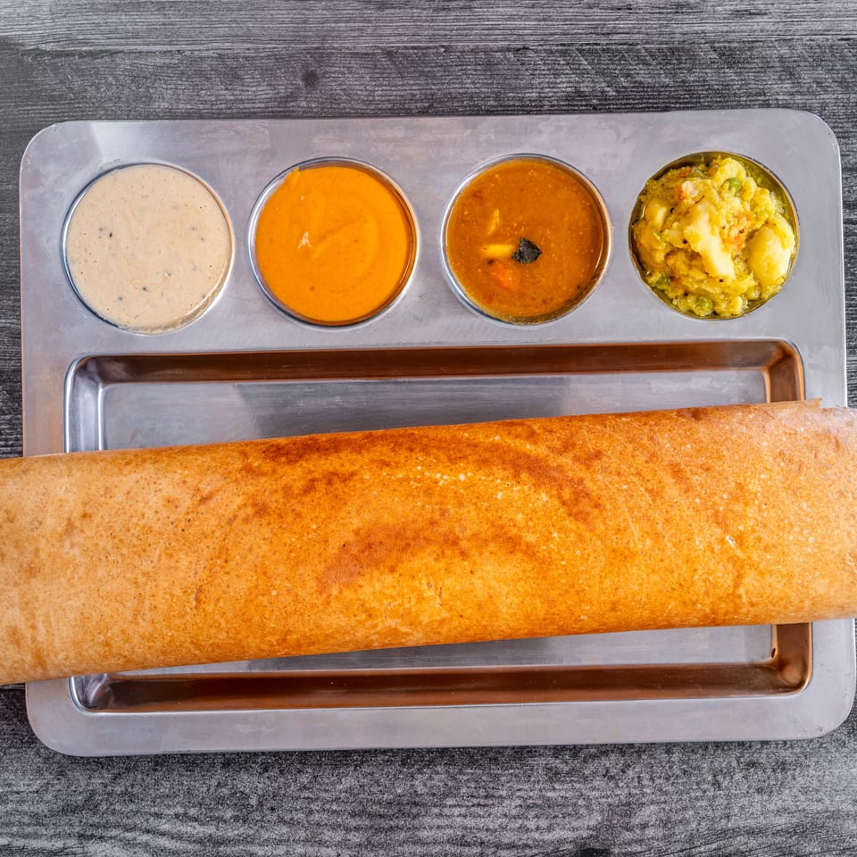 Masala Indian Cuisine's dosa, a crispy crepe, served with four different dipping sauces on a metal tray.