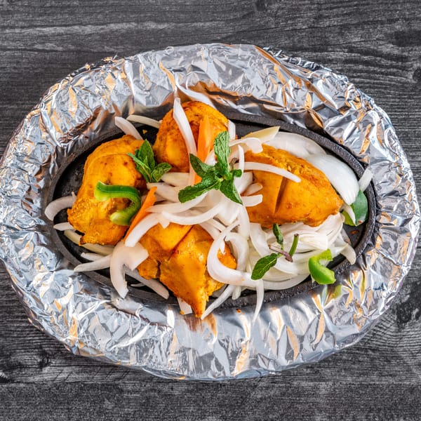 Masala Indian Cuisine's chicken tikka, garnished with sliced onions, bell peppers, and mint, served in a hot skillet.