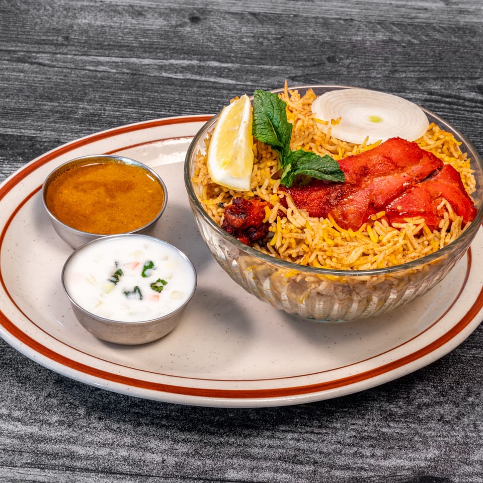 Masala Indian Cuisine's chicken biryani with lemon, mint, onion, and two sauces on a plate.