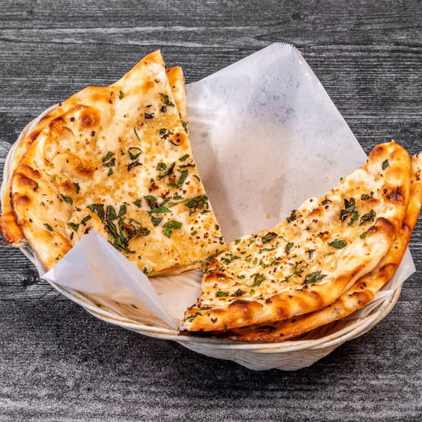 A basket of golden-brown garlic naan bread, garnished with fresh herbs, on a dark wooden table.